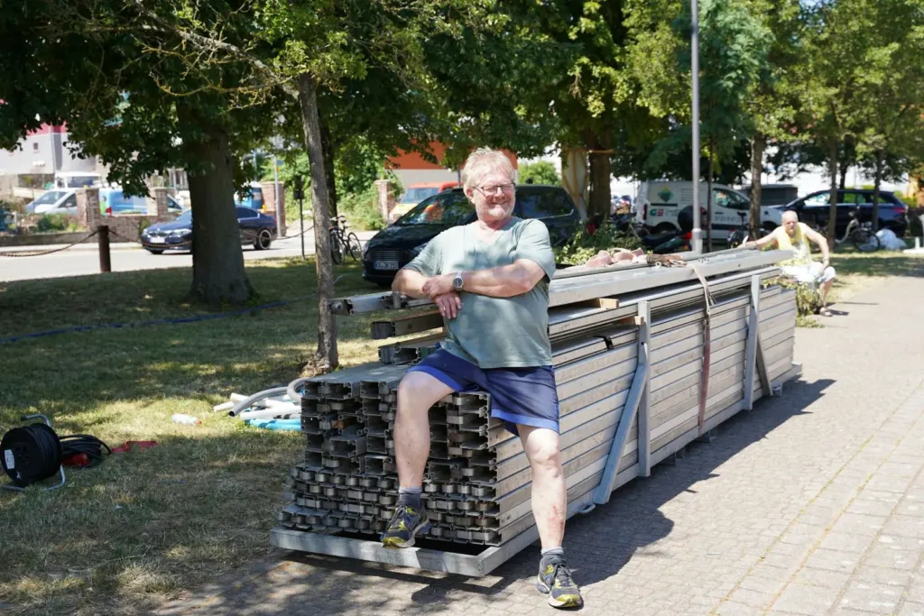 Ein Helfer sitzt lachend auf gestapelten Bühnenelementen beim Aufbau des Festplatzes